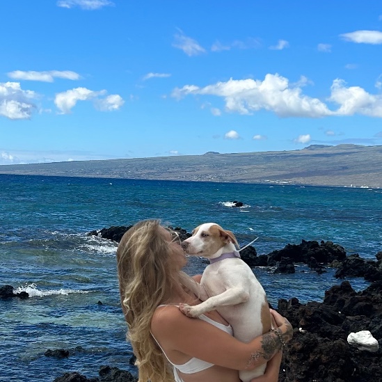 A woman holding her small dog by the ocean on Hawaiʻi Island